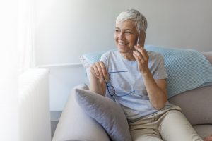 Smiling senior woman using phone sitting on couch at home.